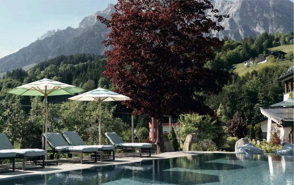 Outdoor pool and sun loungers at Hotel Der Löwe with the Leogang mountains behind